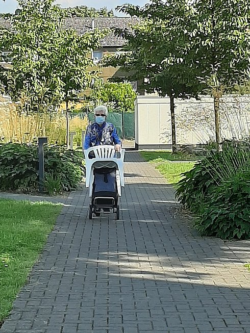 Frau trägt Gartenstuhl durchs Grüne