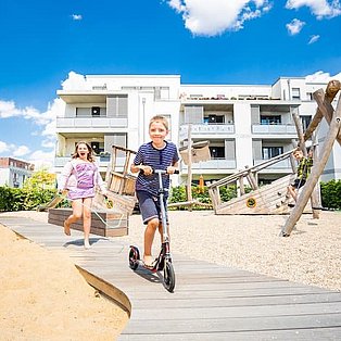 WSG barierrefreier Spielplatz zwei Kinder fahren auf Weg über Spielplatz
