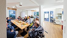 Mietertreff: Personen sitzen am Tisch zusammen, trinken Kaffee, essen und unterhalten sich
