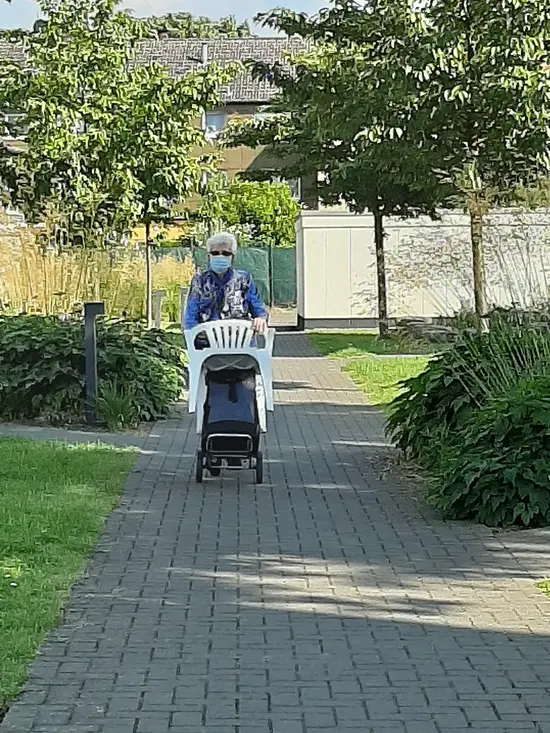 Frau trägt Gartenstuhl durchs Grüne