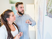 zwei junge Menschen vor Whiteboard mit Bauplänen