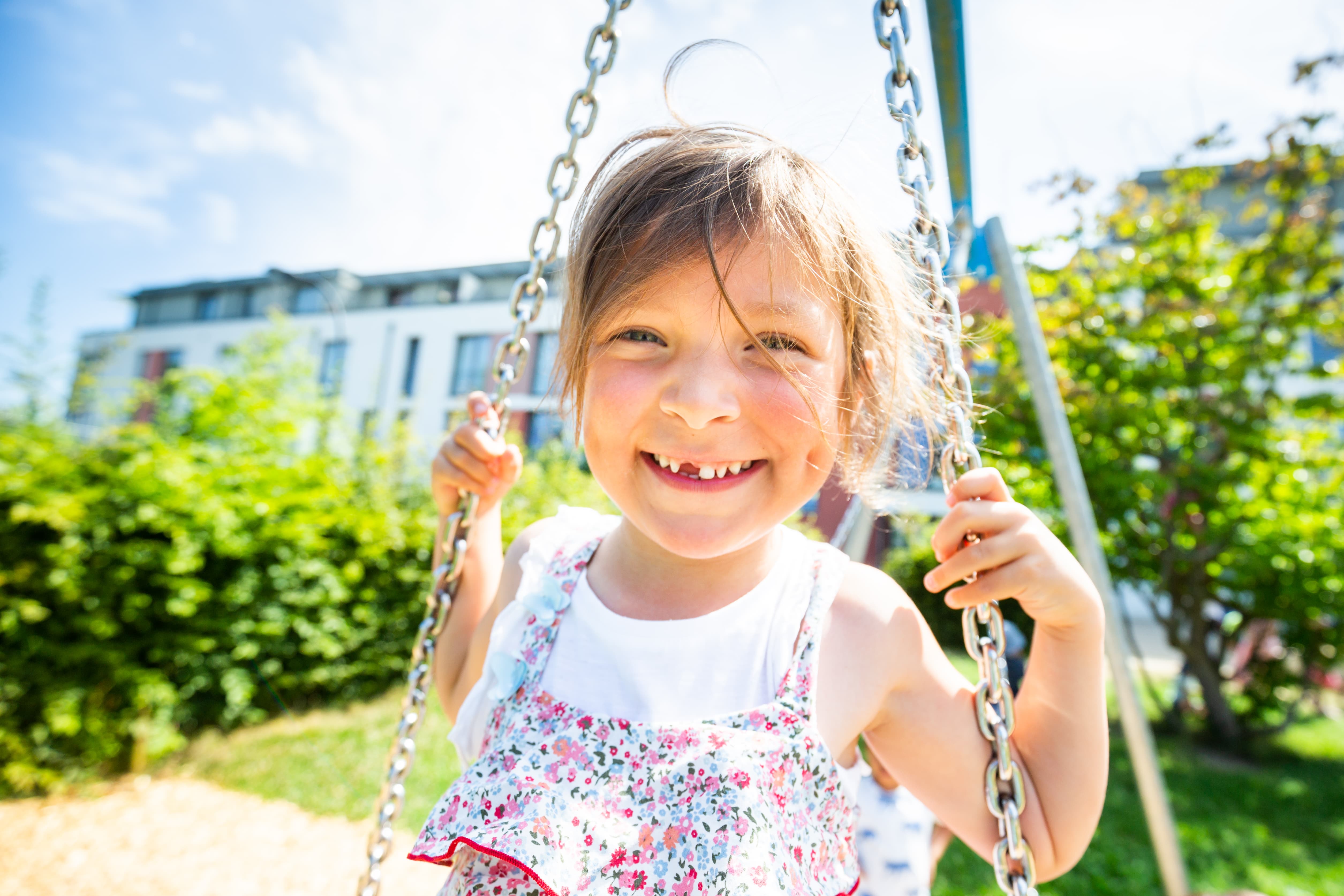 WSG Spielplatz Fröhlich lächelndes kleines Mädchen schaukelt im Hof